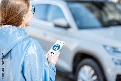 Woman unlocking car using mobile application on a smart phone. Concept of a remote control and car protection through the internet photo