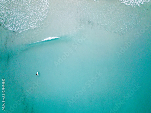 Aerial shot of surfer alone in a wide expance of blue water with waves