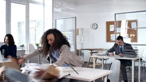 Young businesswoman getting pissed off at work and sweeping stuff off from workplace in office, standing on desk and start dancing with group of excited colleagues