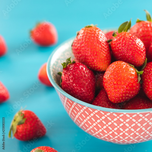 colorful ripe strawberries in a bright bowl on a blue background