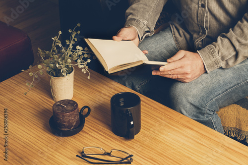 Hombre leyendo un libro con una taza de café sobre una mesa de madera rústica. Vista superior photo