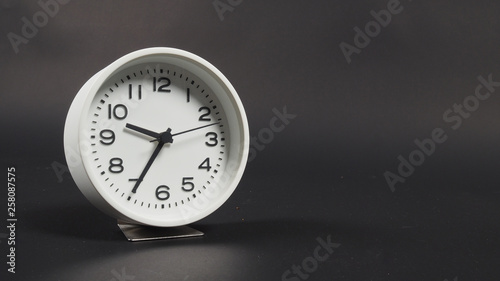 White Alarm clock with hour hand and second hand on black background.
