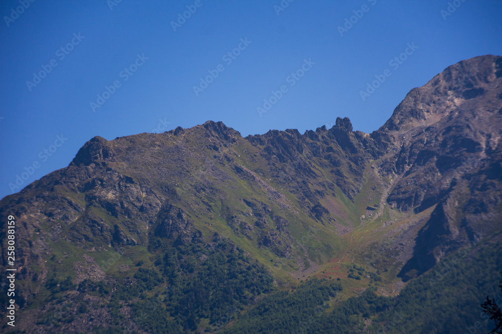 A huge panorama of high Caucasus mountains and beautiful trees on a sunny summer day. A very large amount of stones.