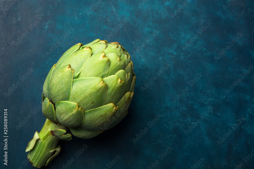 Fototapeta premium Ripe green artichoke on dark blue background. Creative food poster. Minimalist style. Mediterranean Spanish cuisine healthy plant based diet superfoods concept