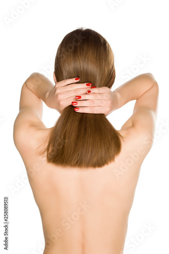 Back view of young nude woman holding her long hair on white background