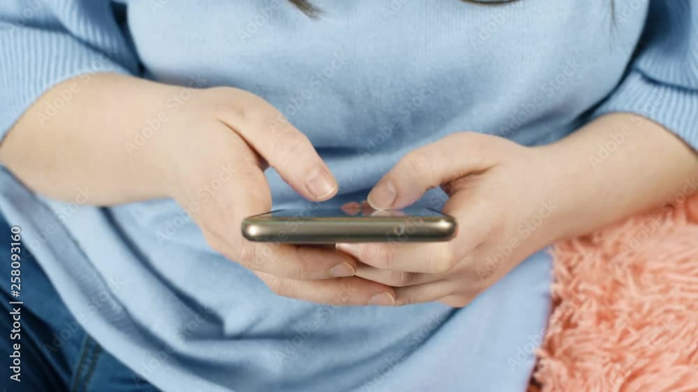 Young girl texting message on smartphone and seat on couch. Close up slow motion. 4K footage. Young girl texting message on smartphone and seat on couch. Close up slow motion. 4K footage.