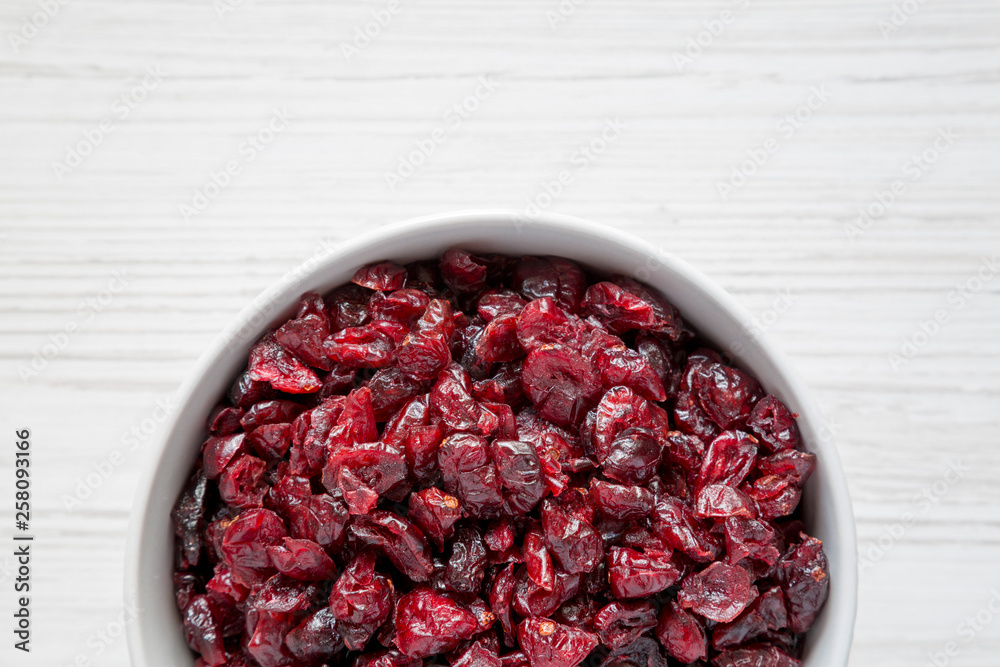 Dried organic cranberries in a bowl over white wooden background, top view. From above, overhead, flat lay. Copy space. Dried organic cranberries in a bowl over white wooden background, top view. From above, overhead, flat lay. Copy space.