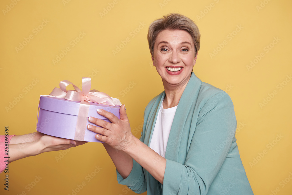 Half length of happy beautiful mother receiving a gift on yellow background Half length of happy beautiful mother receiving a gift on yellow background