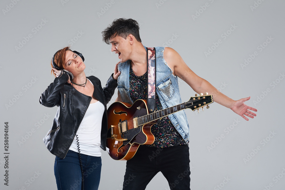 Obraz premium Musical artists sing and play electric guitar. Contemporary cover band. Isolated over grey background. Woman and man with headphones sing loudly