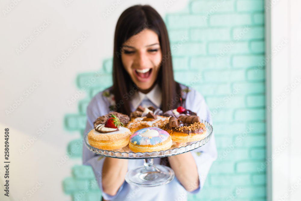 Beautiful young woman enjoying in delicious glazed and decorated donuts
