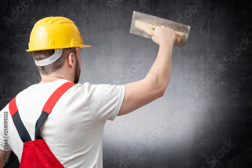 Rear view of a worker plastering a wall indoors