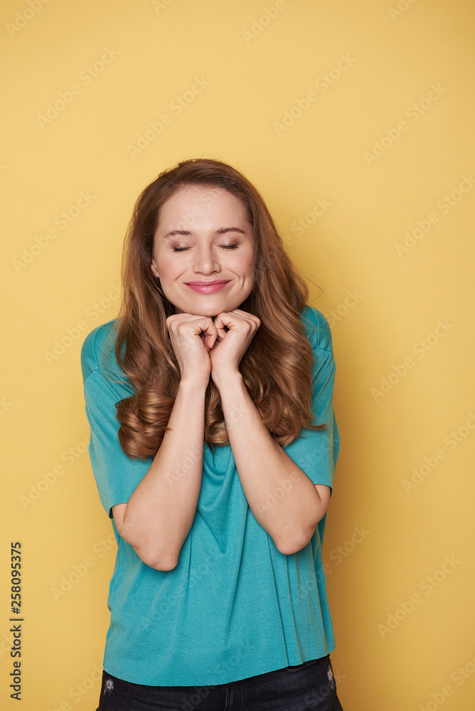 Brown-haired smiling girl with closed eyes making wish on yellow background