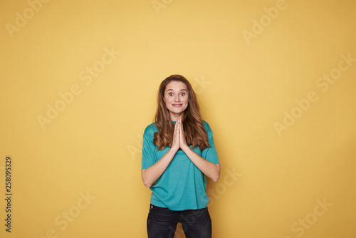 Portrait of brown-haired surprised smiling girl meditating on yellow background