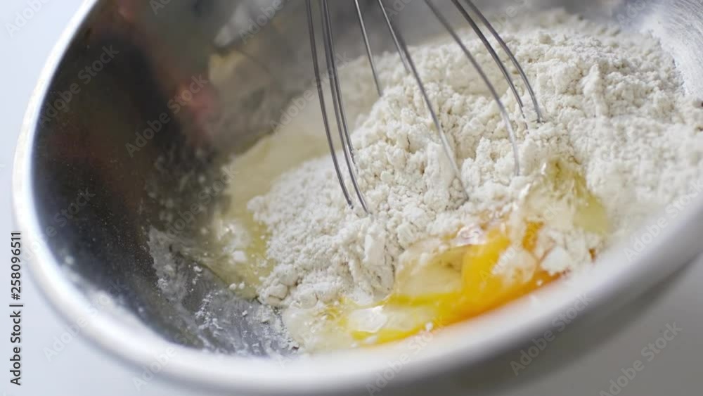 Slow motion crop shot of woman preparing homemade omelette mixing with whisk eggs.