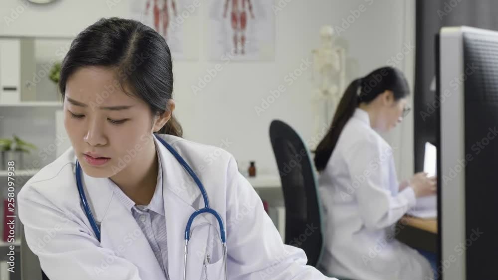 Stressed female doctor sat at office desk in hospital. young asian girl healthcare worker working long hours. Overworked medical staff at desktop confused frowning looking at computer screen. Stressed female doctor sat at office desk in hospital. young asian girl healthcare worker working long hours. Overworked medical staff at desktop confused frowning looking at computer screen.