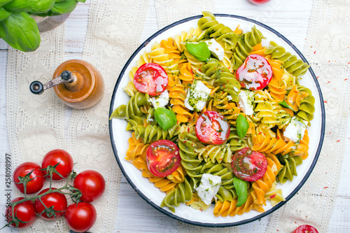 Italian food - Salad with colorful pasta, cherry tomatoes, feta cheese and fresh basil on white wooden background