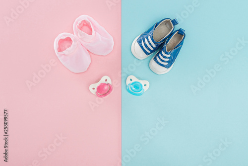 top view of pacifiers, booties, sneakers on pink and blue background with copy space