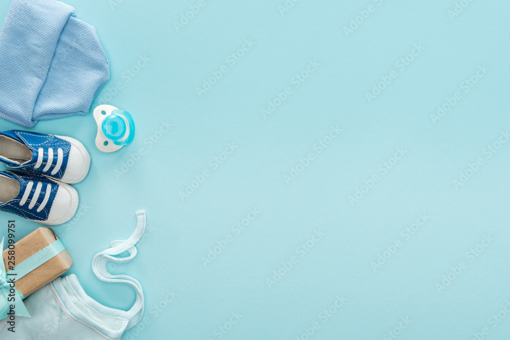 top view of pacifier, gift, sneakers, bonnet, hat on blue background with copy space - obrazy, fototapety, plakaty 