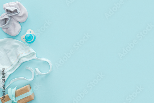 top view of pacifier, gift, bonnet, booties on blue background with copy space