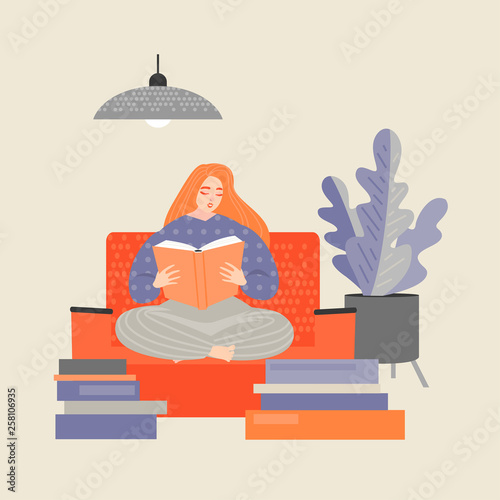 Red-haired girl sitting on the couch and reading a book