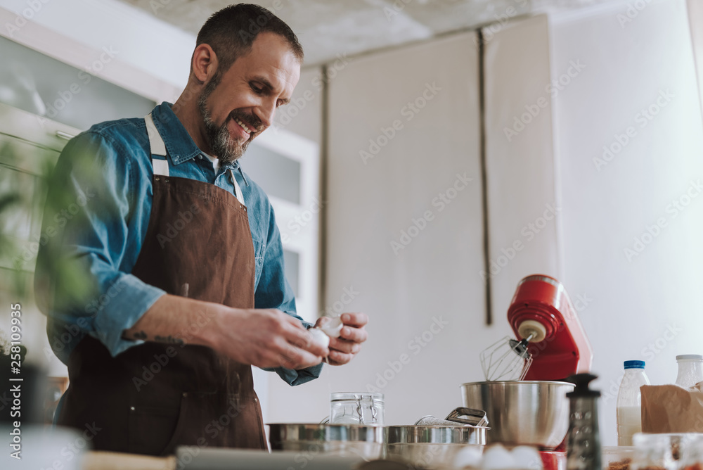 Bearded man smiling while looking at the cracked egg Bearded man smiling while looking at the cracked egg