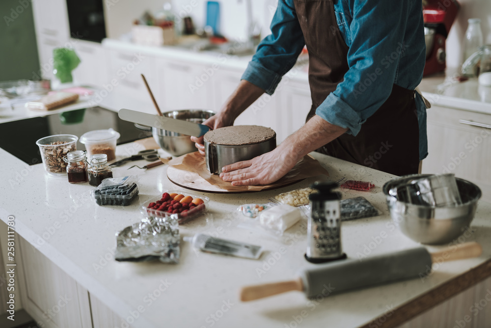 Hands holding cake icing spreader near the cake in shape Hands holding cake icing spreader near the cake in shape
