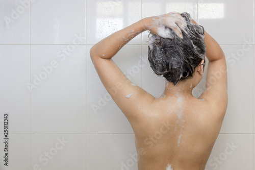 Young asian woman taking a shower and washing hair in white bathroom
