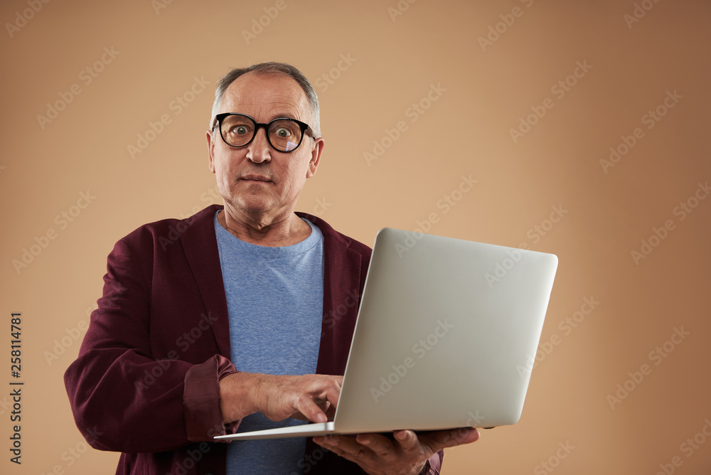 Astonished adult man looking at the camera while standing with laptop Astonished adult man looking at the camera while standing with laptop