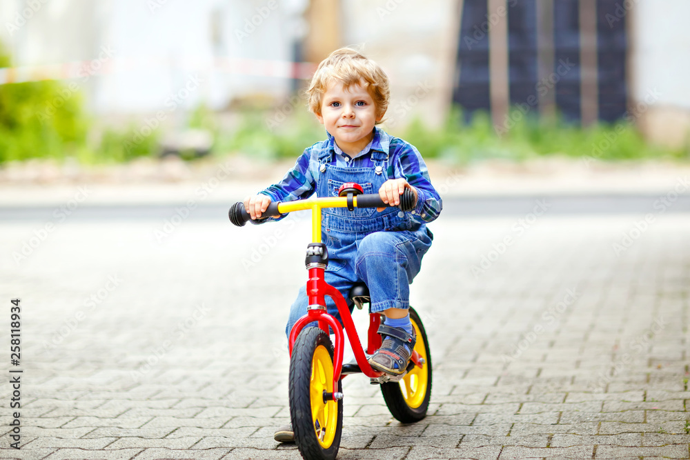 Active blond kid boy in colorful clothes driving balance and learner's bike or bicycle in domestic garden. Toddler child dreaming and having fun on warm summer day. outdoors movement game for children Active blond kid boy in colorful clothes driving balance and learner's bike or bicycle in domestic garden. Toddler child dreaming and having fun on warm summer day. outdoors movement game for children