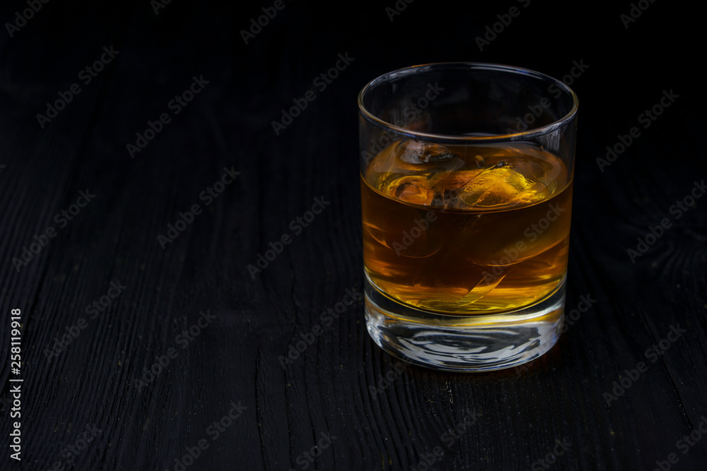 A glass of whisky with ice on the ebony table.