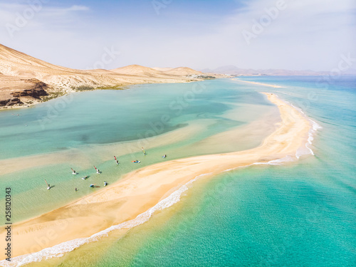 Aerial view of beach in Fuerteventura island with windsurfers learning windsurfing in blue turquoise water during summer vacation holidays, Canary islands from drone photo