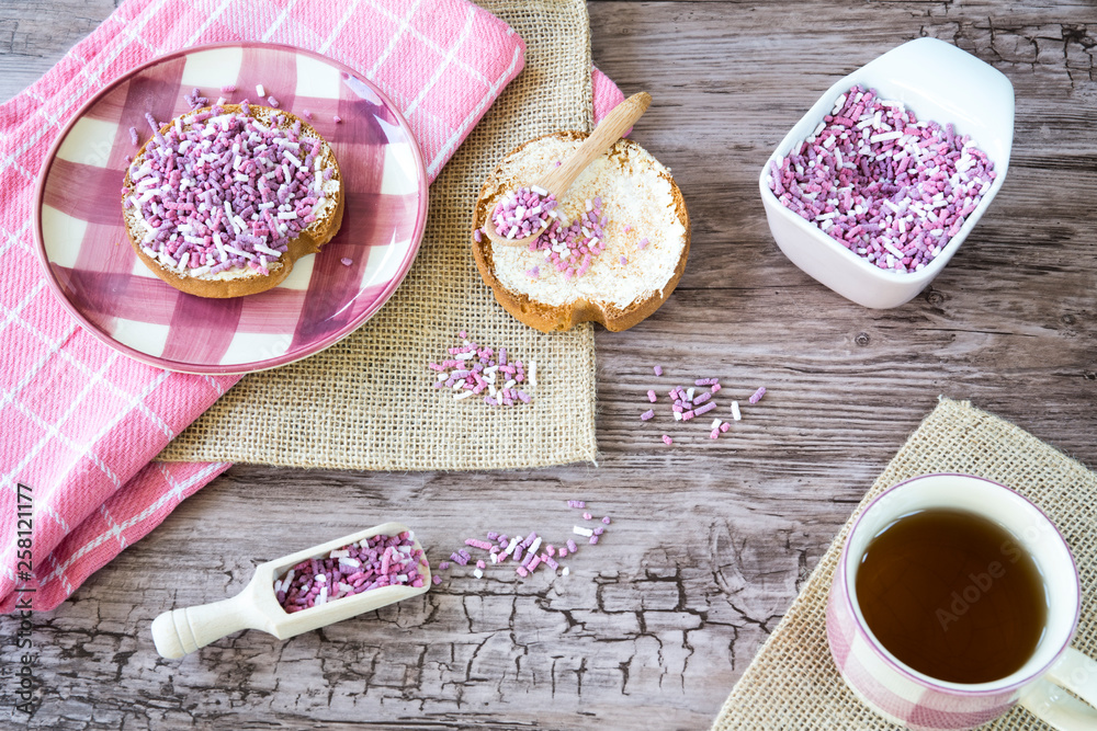 decorative flat lay, Dutch breakfast with cup of tea, rusk with pink sweet sprinkles, hail on plate on wooden table