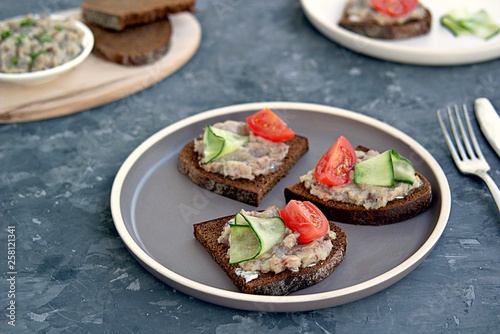 Open sandwiches on rye bread with forshmak, a snack of chopped salted herring, onions and eggs on a ceramic plate. Decorated with sliced fresh cucumbers and tomatoes.