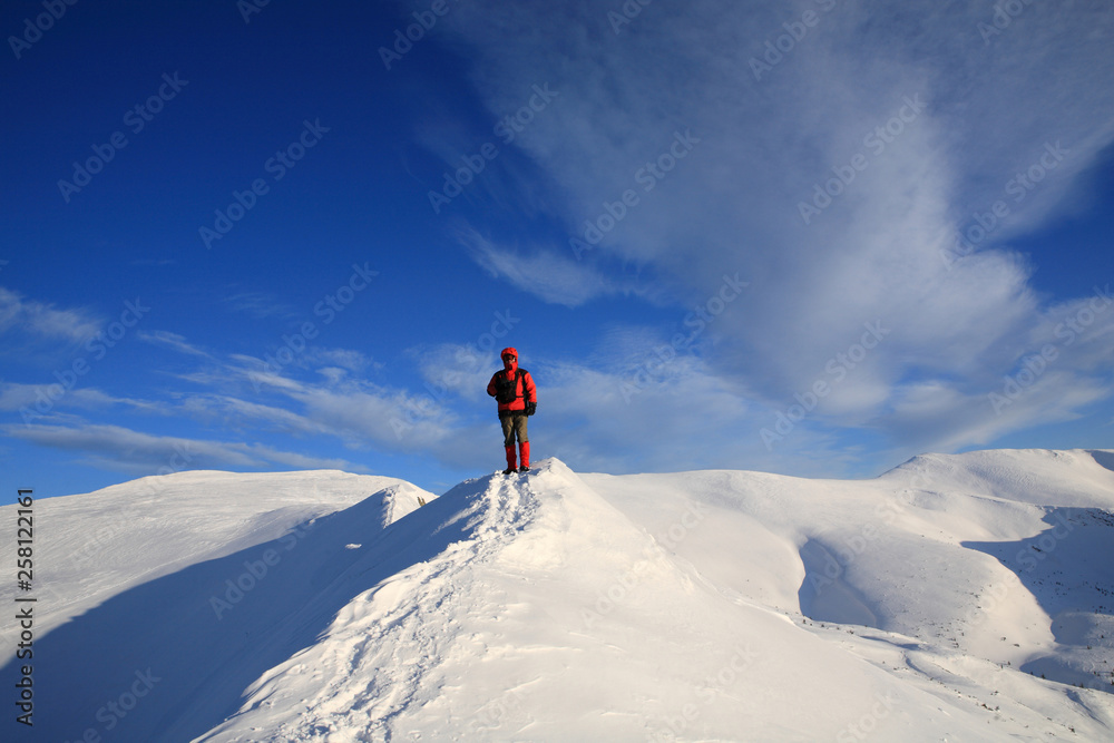 The tourist stands on the ridge of the mountains in the winter mountains