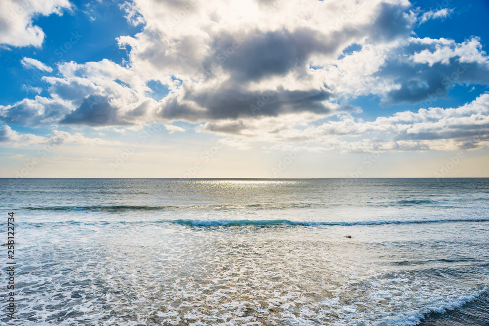 Seascape with silver sunlight reflection, calm waves, bright sky and white clouds