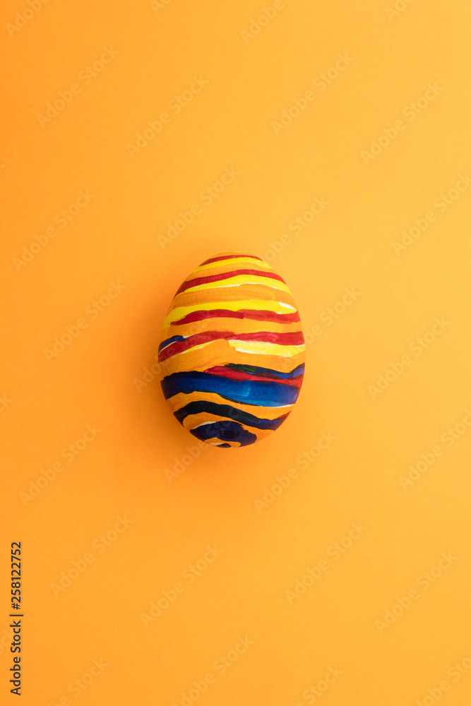 Detail of painted yellow Easter egg with red and blue stripes in orange background