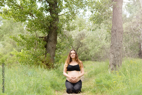 Pregnant beautiful woman yoga outdoors on the grass in sunny summer day