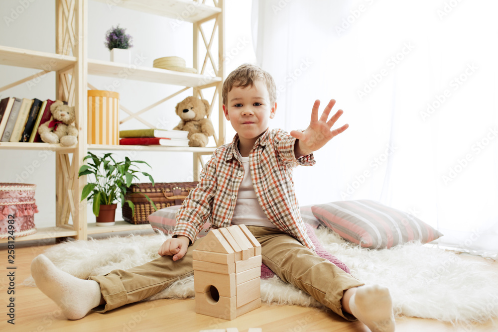 Little child sitting on the floor. Pretty boy palying with wooden cubes at home. Conceptual image with copy or negative space and mock-up for your text Little child sitting on the floor. Pretty boy palying with wooden cubes at home. Conceptual image with copy or negative space and mock-up for your text