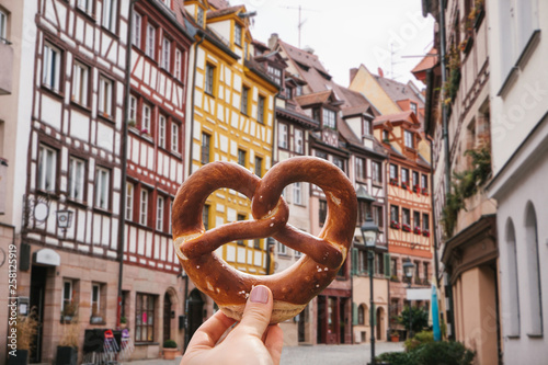Fotografie A girl holds in her hand a traditional German pretzel on the background of a beautiful architecture or street in Nuremberg in Germany