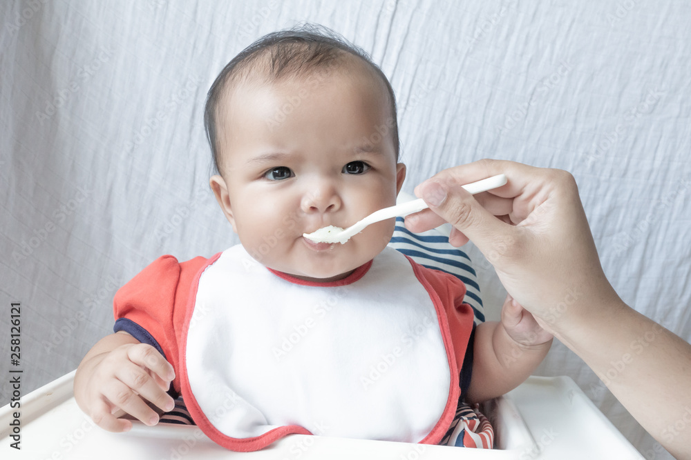 Baby girl eating food on white high chair Baby girl eating food on white high chair