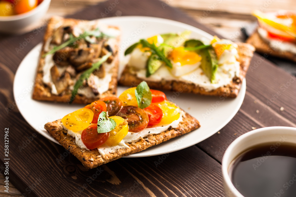 Breakfast table with tasty bruschetta crostini toasts, cream cheese, fresh vegetables and fruits and a cup of black coffee. Morning heathy balanced diet. Colorful ingredients on rustic wood background Breakfast table with tasty bruschetta crostini toasts, cream cheese, fresh vegetables and fruits and a cup of black coffee. Morning heathy balanced diet. Colorful ingredients on rustic wood background