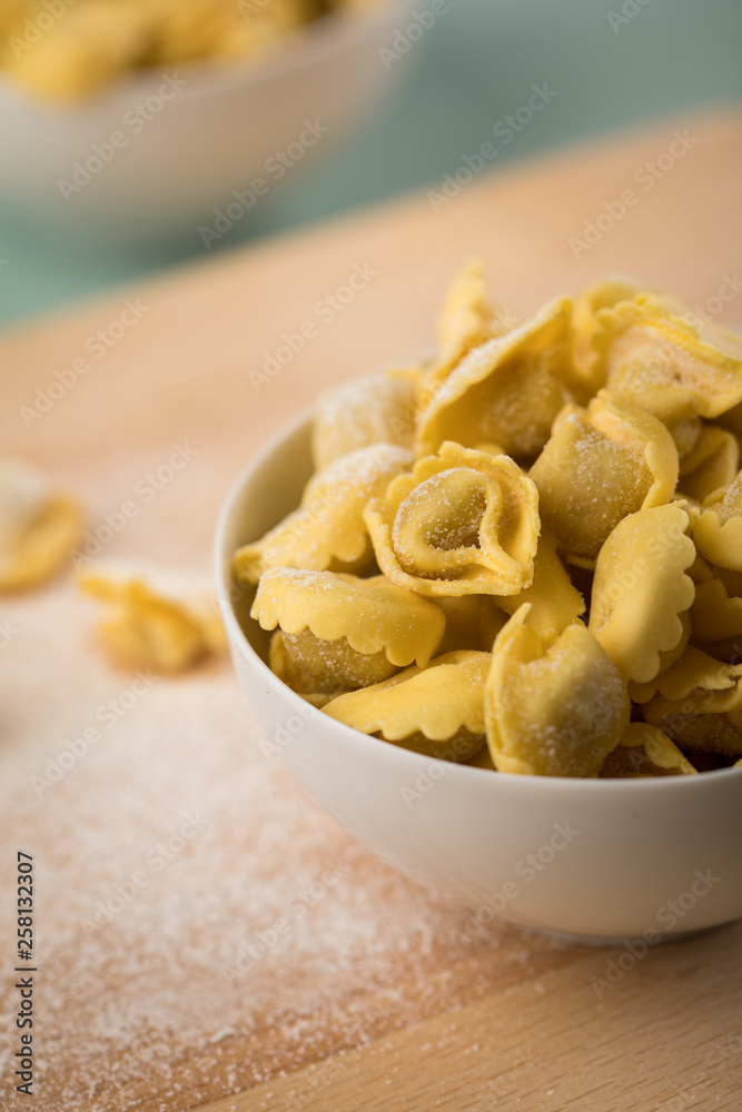 Frische, rohe Cappelletti Tortellini Pasta mit Mehl und Grieß in Porzellan Schale auf Holz Brett und Pastell Grün Hintergrund