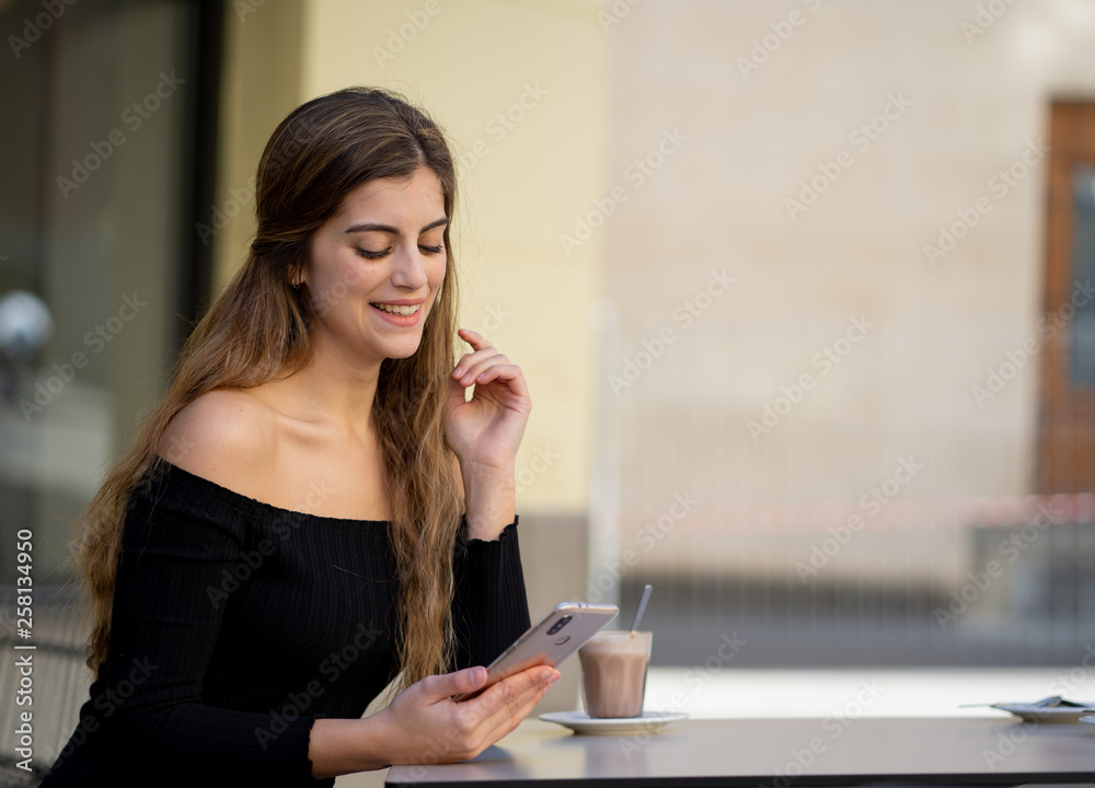 Attractive young woman chatting and dating on smart mobile phone in coffee shop outside city street