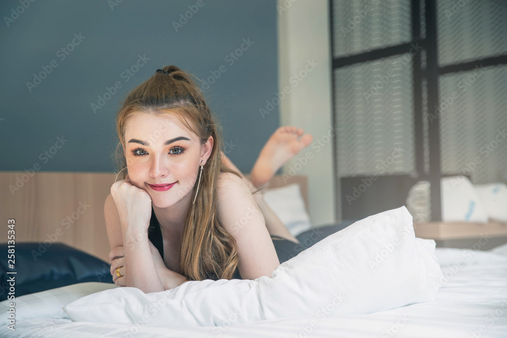 Beautiful young woman on bed in modern apartment smiling after wake up. Woman is relaxing on comfortable bed at bedroom in the morning. Beautiful young woman on bed in modern apartment smiling after wake up. Woman is relaxing on comfortable bed at bedroom in the morning.