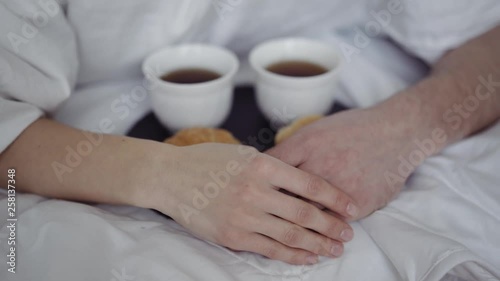breakfast with coffee and fresh croissants, on table, happy couple hiding under a blanket and hold hands. Happy morning