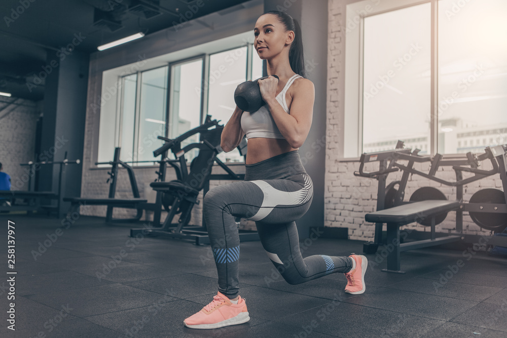 Low angle shot of a sporty young woman doing lunges with kettlebell. Attractive sportswoman enjoying working out at the gym, copy space. Fitness female in sportswear training with weights Low angle shot of a sporty young woman doing lunges with kettlebell. Attractive sportswoman enjoying working out at the gym, copy space. Fitness female in sportswear training with weights