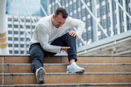 Canvas Print fitness man have knee pain sitting on steps of stair in the city