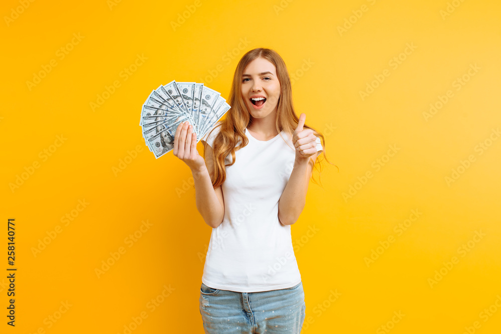 Portrait of a happy contented girl holding a pile of banknotes and looking at the camera on a yellow background Portrait of a happy contented girl holding a pile of banknotes and looking at the camera on a yellow background