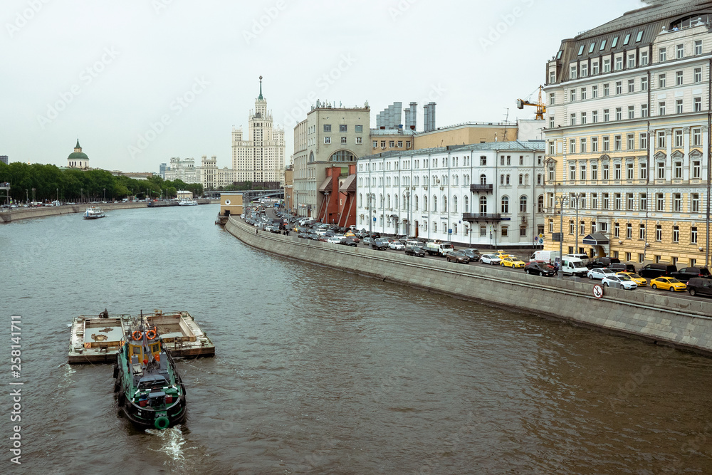 Obraz premium Stalin skyscraper on the background of the river with a boat. Moscow River view of the Stalinist skyscraper. cargo boat runs on the Moscow River