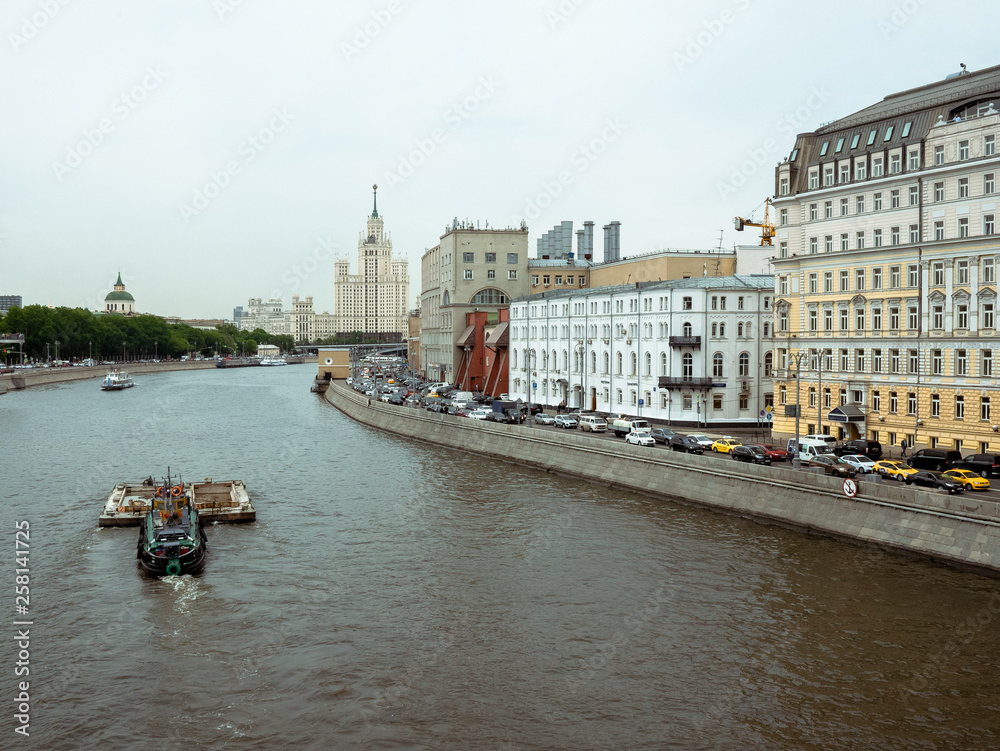 Obraz premium Stalin skyscraper on the background of the river with a boat. Moscow River view of the Stalinist skyscraper. cargo boat runs on the Moscow River